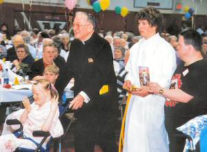 photo of Msgr. Tom Campion, Mary Jane Simdon (in wheelchair) and Scott Peters, right, bringing up Offertory gifts